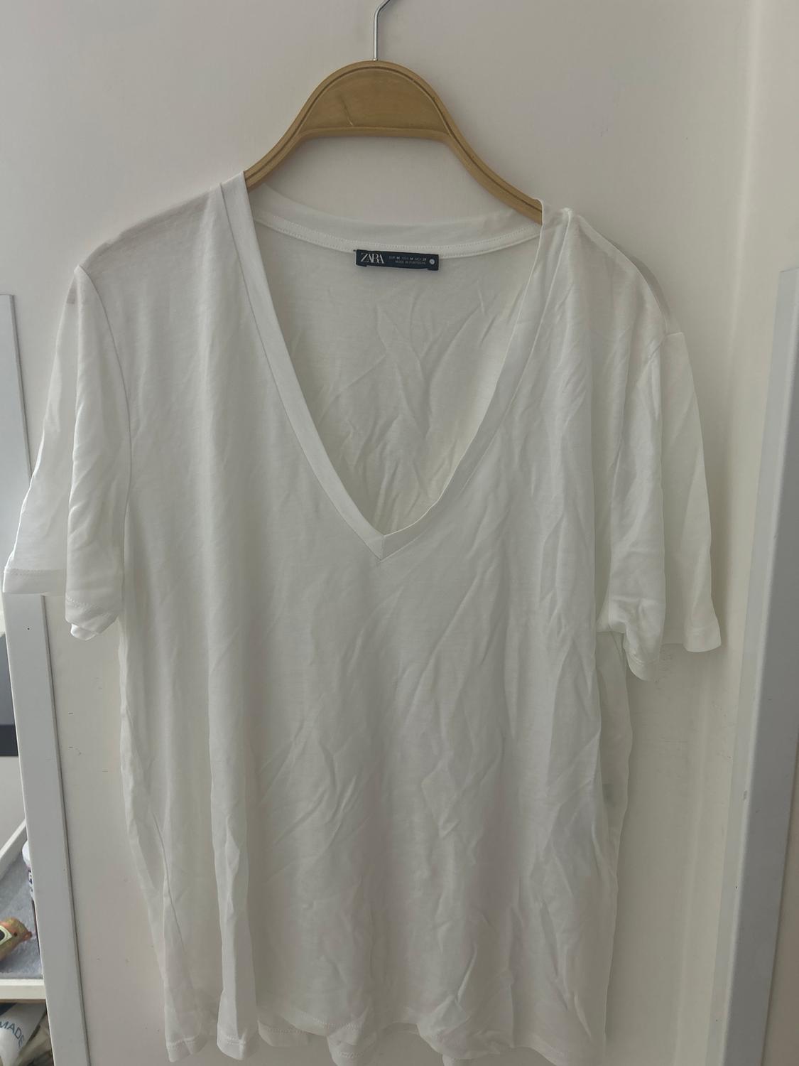 White short-sleeved V-neck t-shirt hanging on a wooden hanger. Visible label with "ZARA" text.