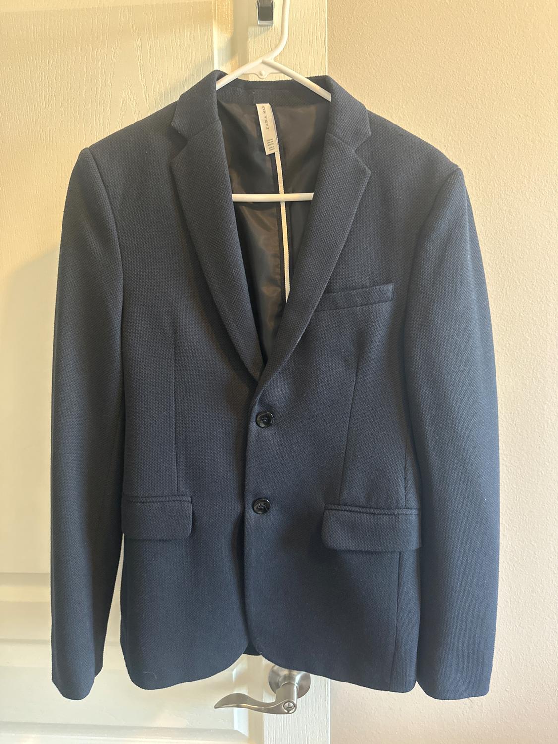 Navy blue jacket hanging on a white hanger over a door. It has classic lapels and two front buttons.