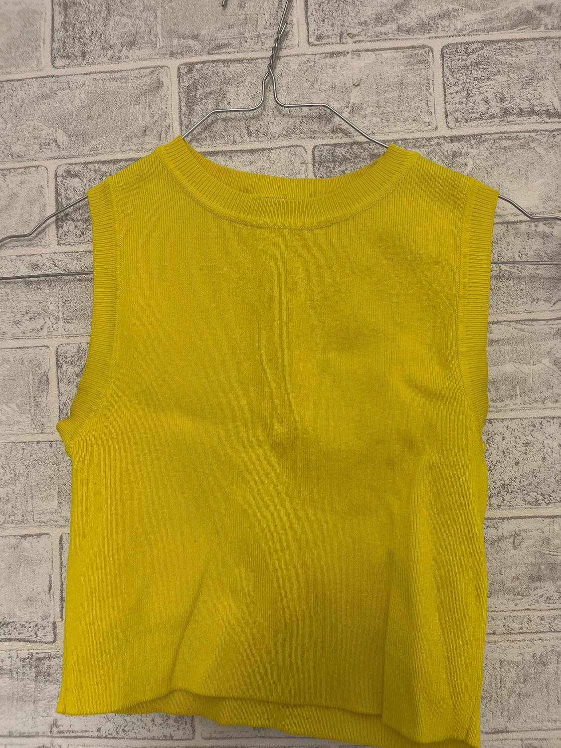 Yellow sleeveless vest hanging on a wire hanger, against a light grey brick wall background.
