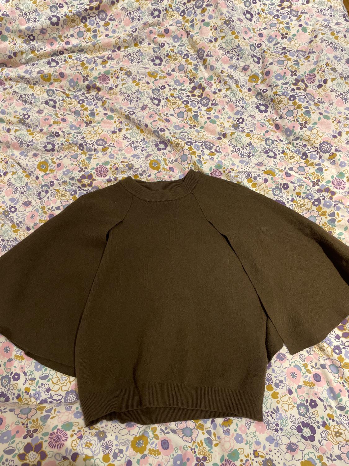 Brown wide-sleeved jumper over colourful floral fabric with pastel-toned flowers and a white background.