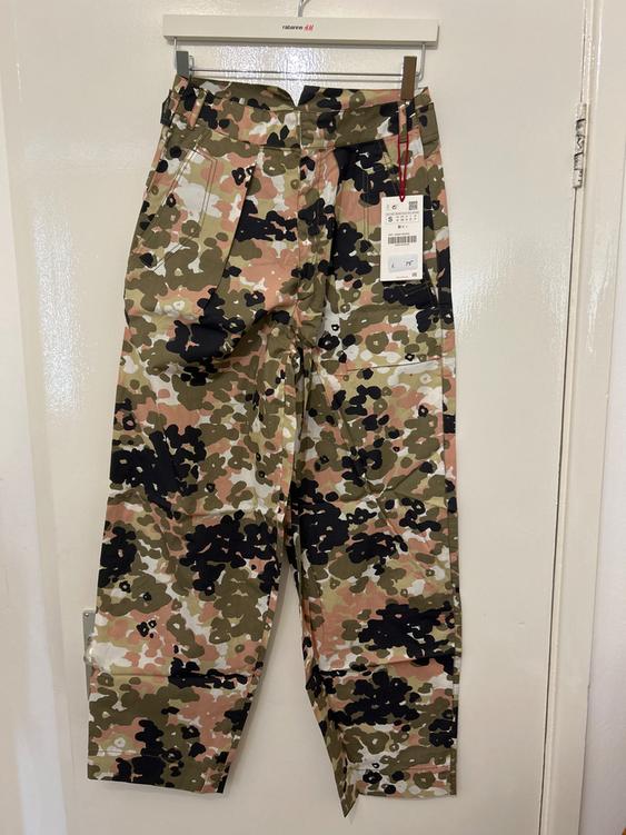 Camouflage trousers hung on a white hanger with a visible price tag. White background.
