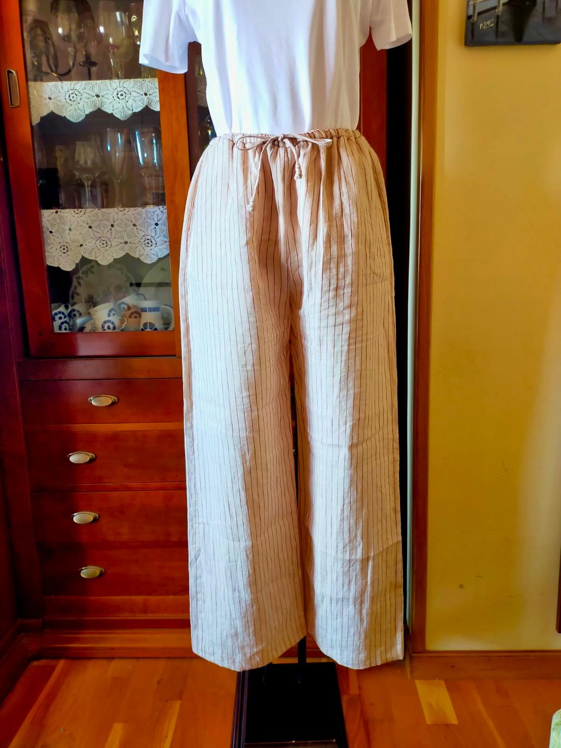 Mannequin in a white T-shirt and beige pinstriped trousers in a home setting with wooden furniture.