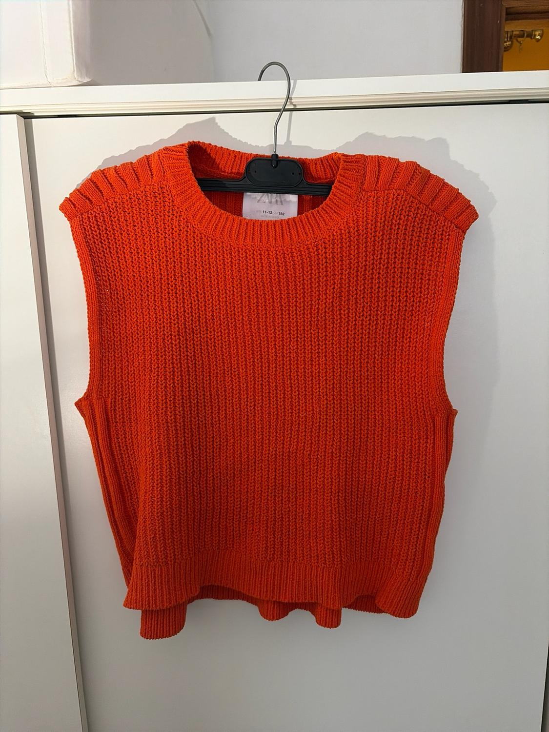 Orange sleeveless knitted waistcoat hanging on a hanger against a white background. Text: ZARA 11-12 cm 152.
