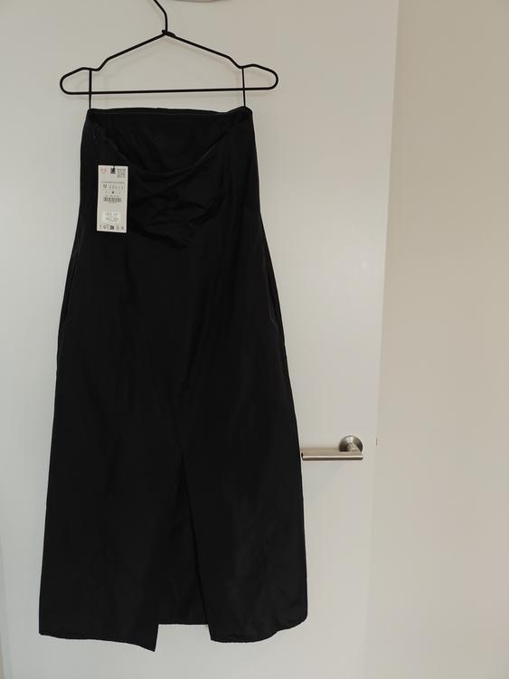 Black dress hanging on a hanger over a white door. Visible tag with product details.