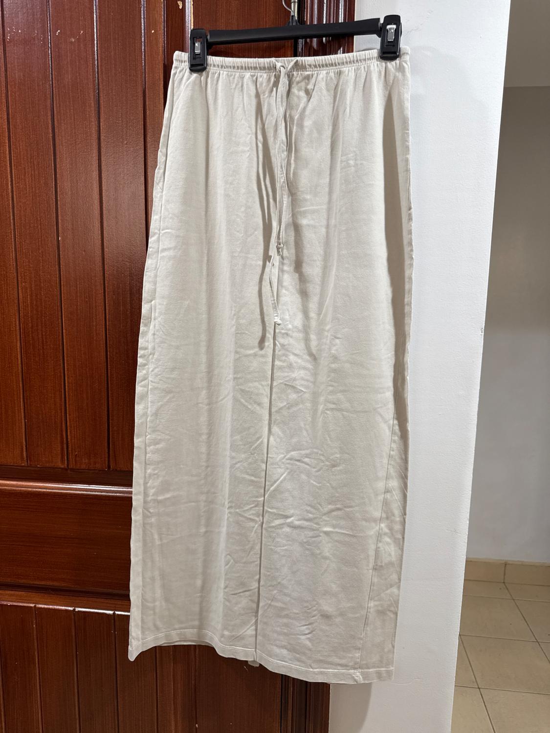 Beige maxi skirt hanging on a black hanger in front of a wooden door. Lightweight fabric with adjustable drawstring at the waist.