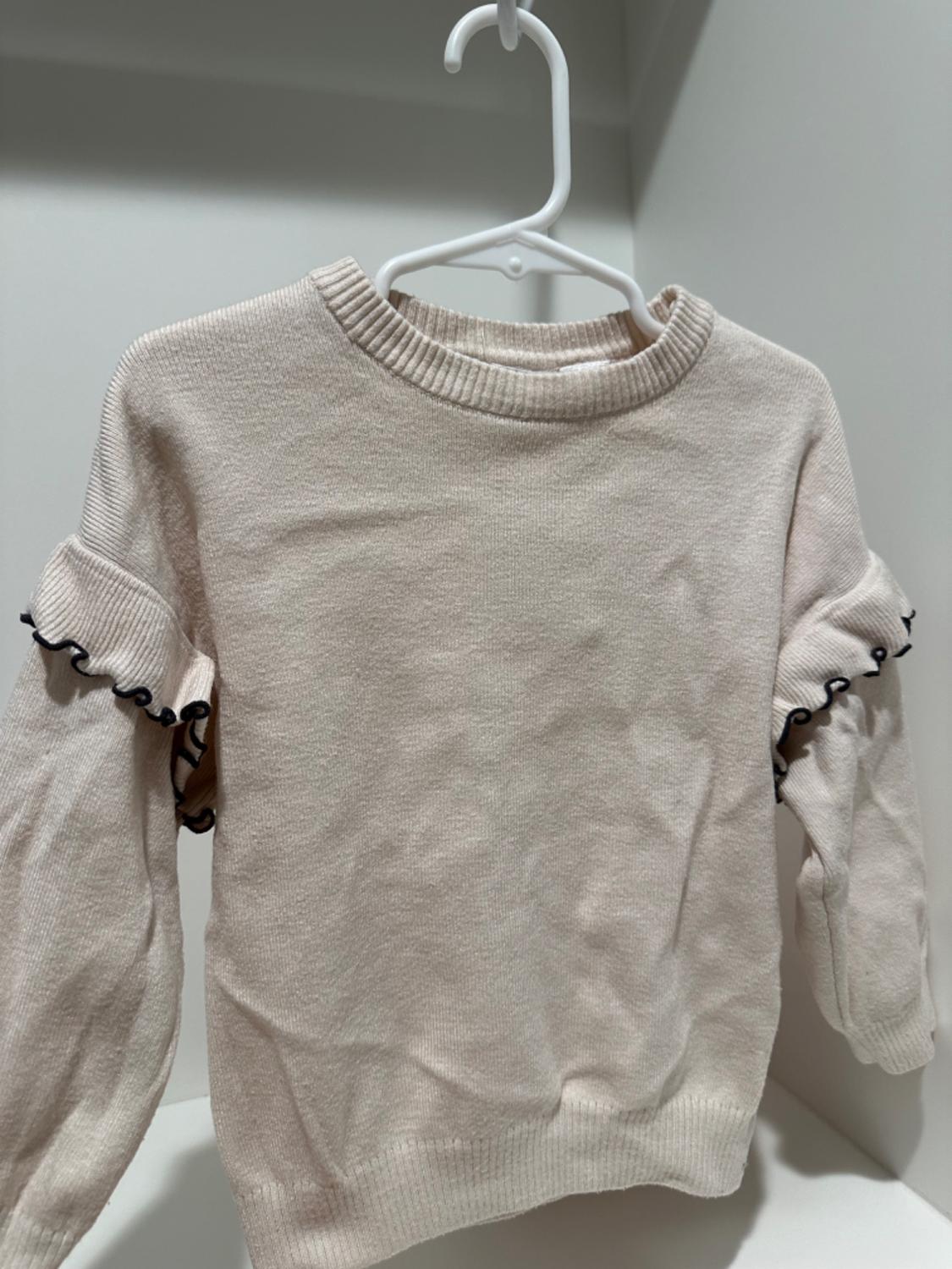 Front view of beige sweater with ruffled sleeves and a round neck.