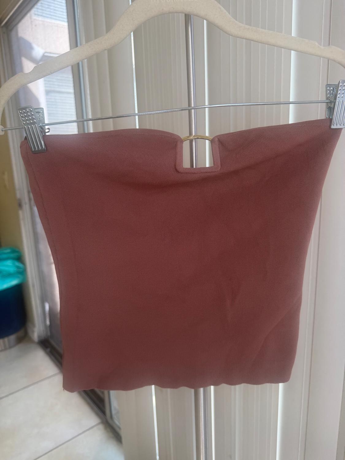 Pink strapless top hanging on a white hanger, with a background of sliding glass doors and vertical blinds.