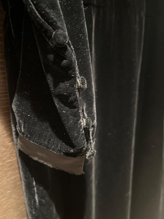 Detail of a black velvet garment with covered buttons, showing texture and stitching in a dark setting.