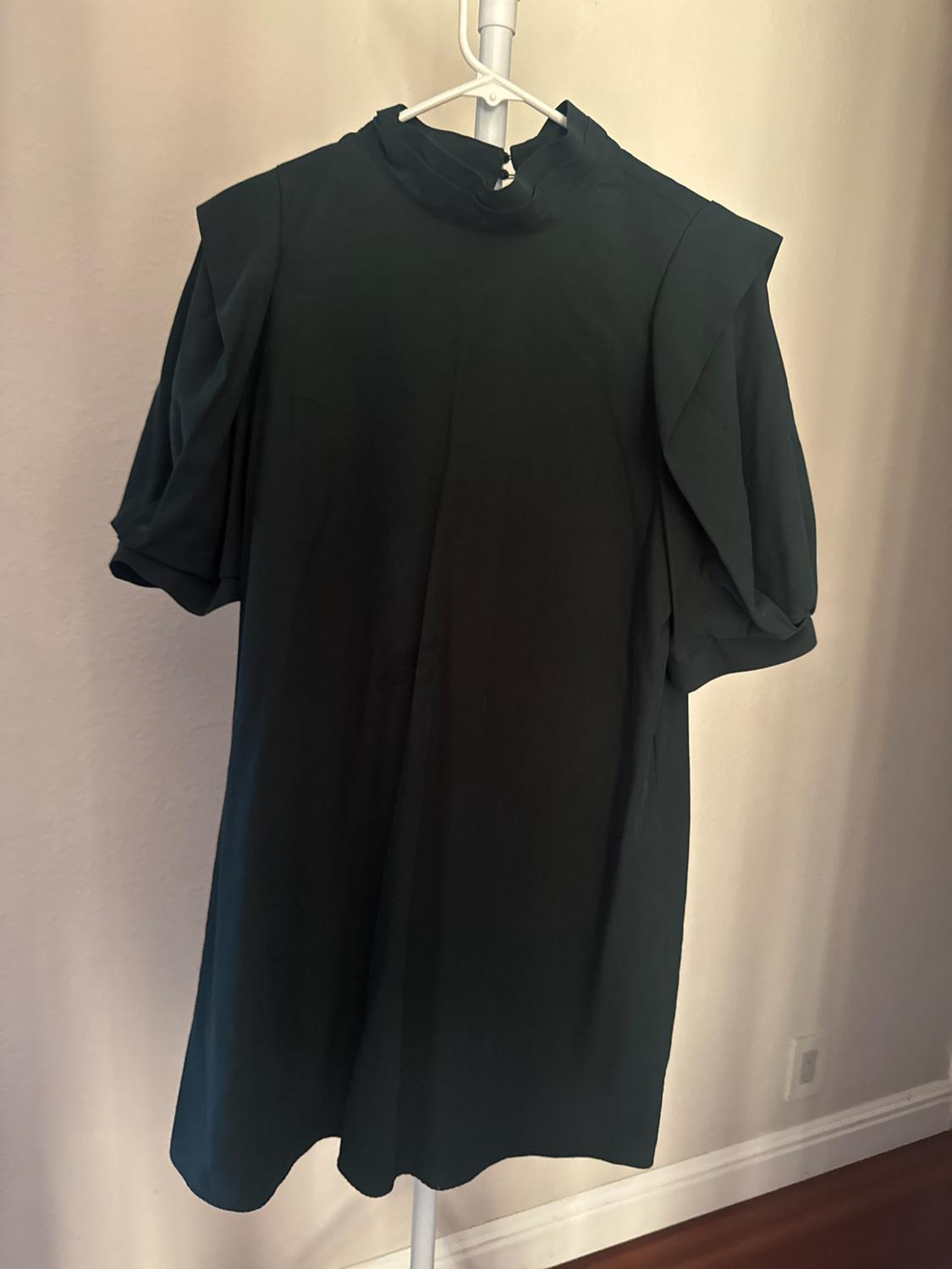 Dark green short dress with a high neck and short puff sleeves, hanging on a white hanger against a light wall.