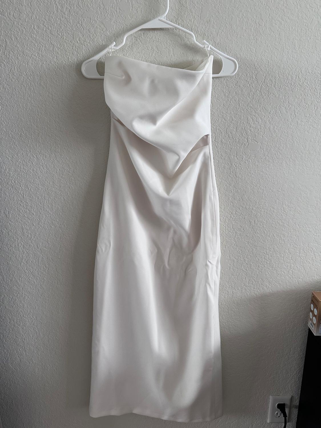 Strapless white dress hanging on a white hanger against a textured wall. The dress features a draped design at the neckline.