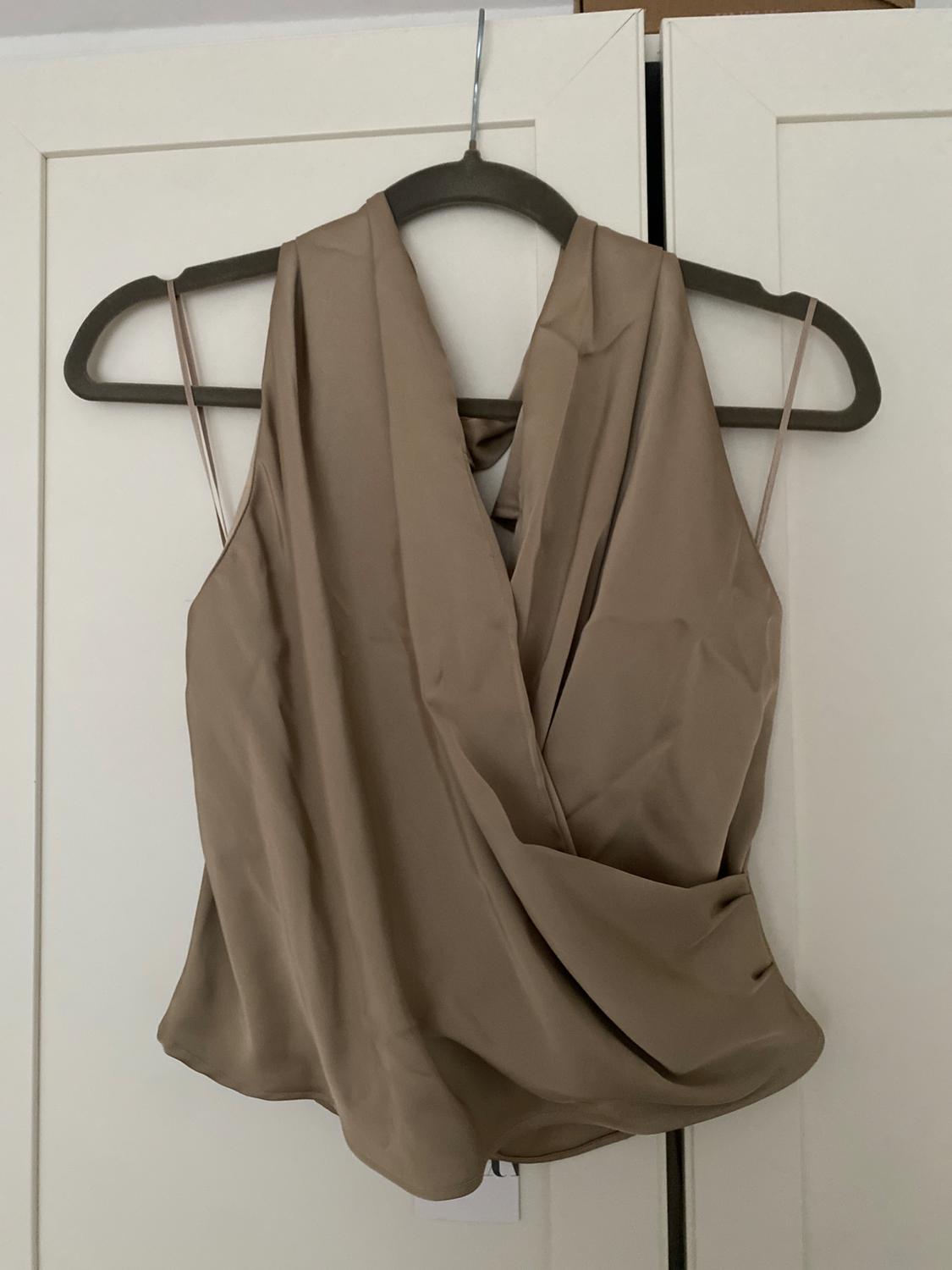 Beige sleeveless top with a crossover neckline, hanging on a black hanger in front of a white door.