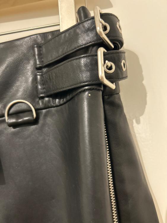 Detail of a black jacket with zips and silver buckles. The material's texture is visible in close-up.