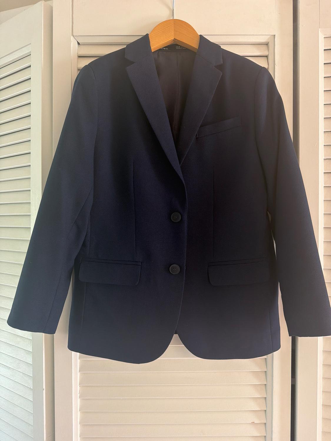 Navy blue jacket hanging on a wooden hanger in front of white shuttered doors.