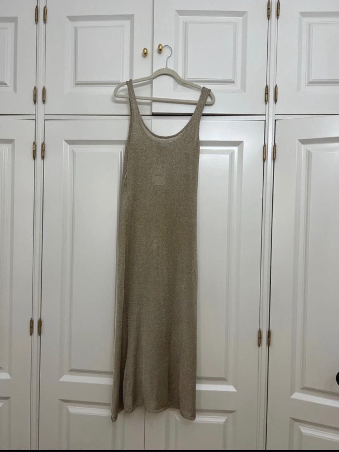 Beige sleeveless knitted maxi dress hanging on a hanger on the doors of a white wardrobe with gold handles.