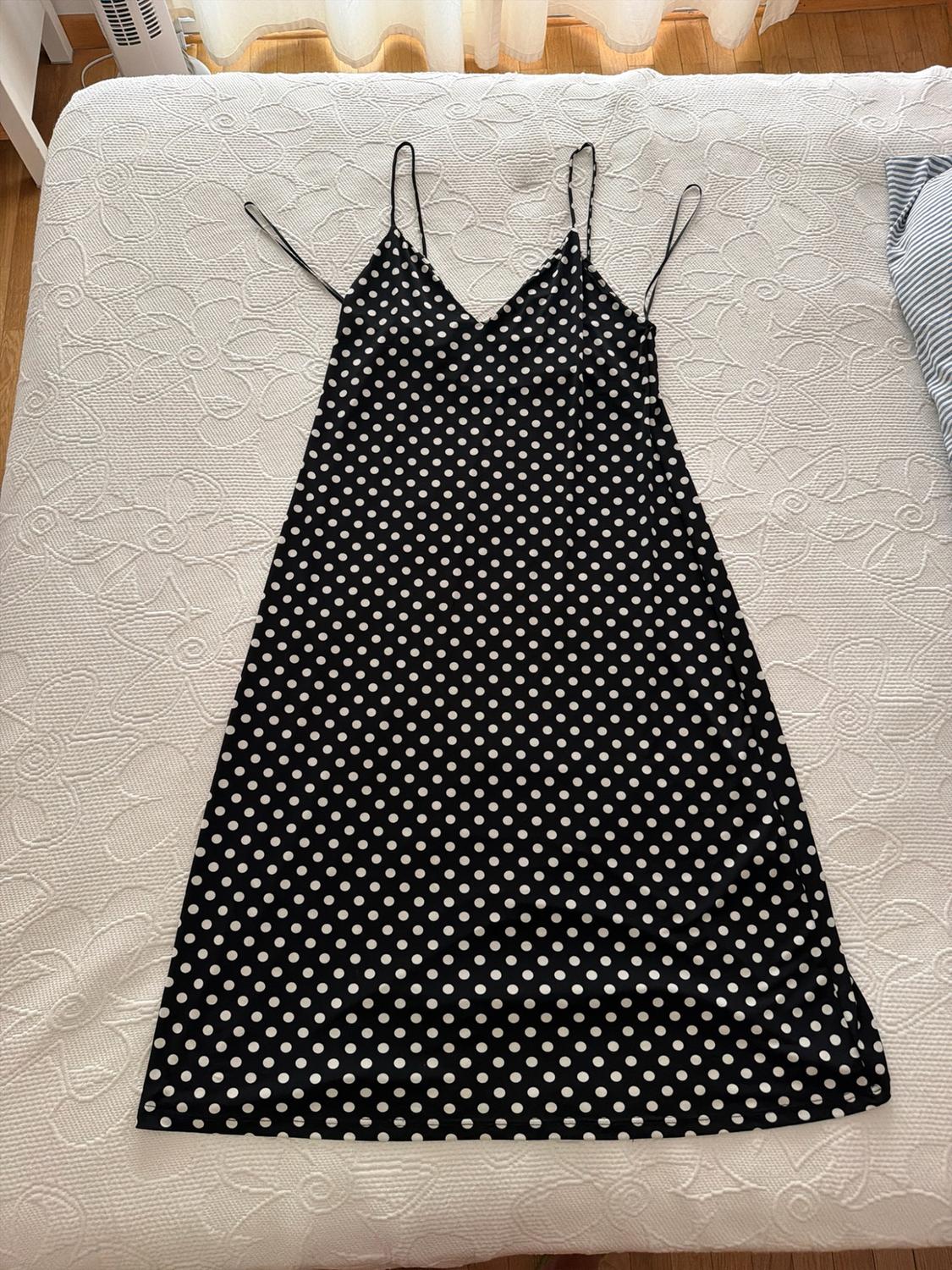 Black polka-dot dress with thin straps, laid out on a bed with a white bedspread in a relaxed home setting.