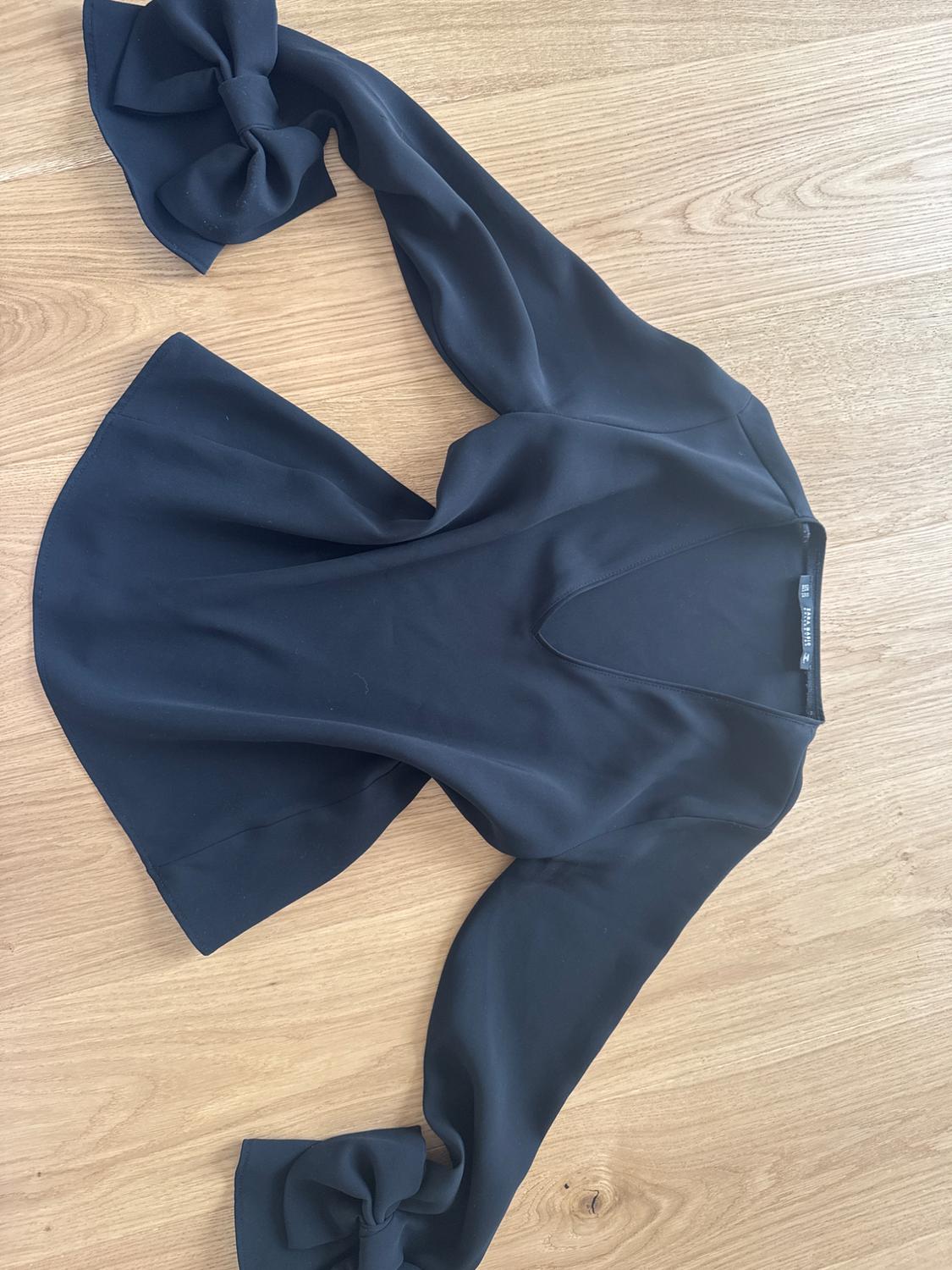 Black long-sleeved blouse with large bows on the cuffs, on a light wooden surface.