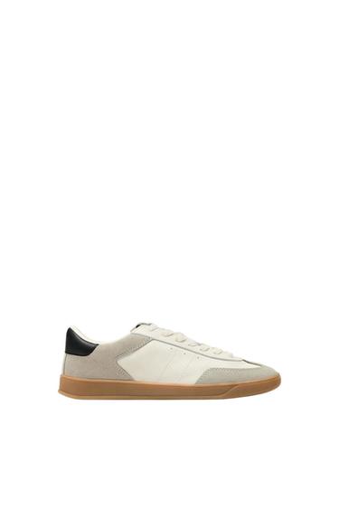 White sports trainers with grey details and a brown sole. Black heel. Minimalist white background.