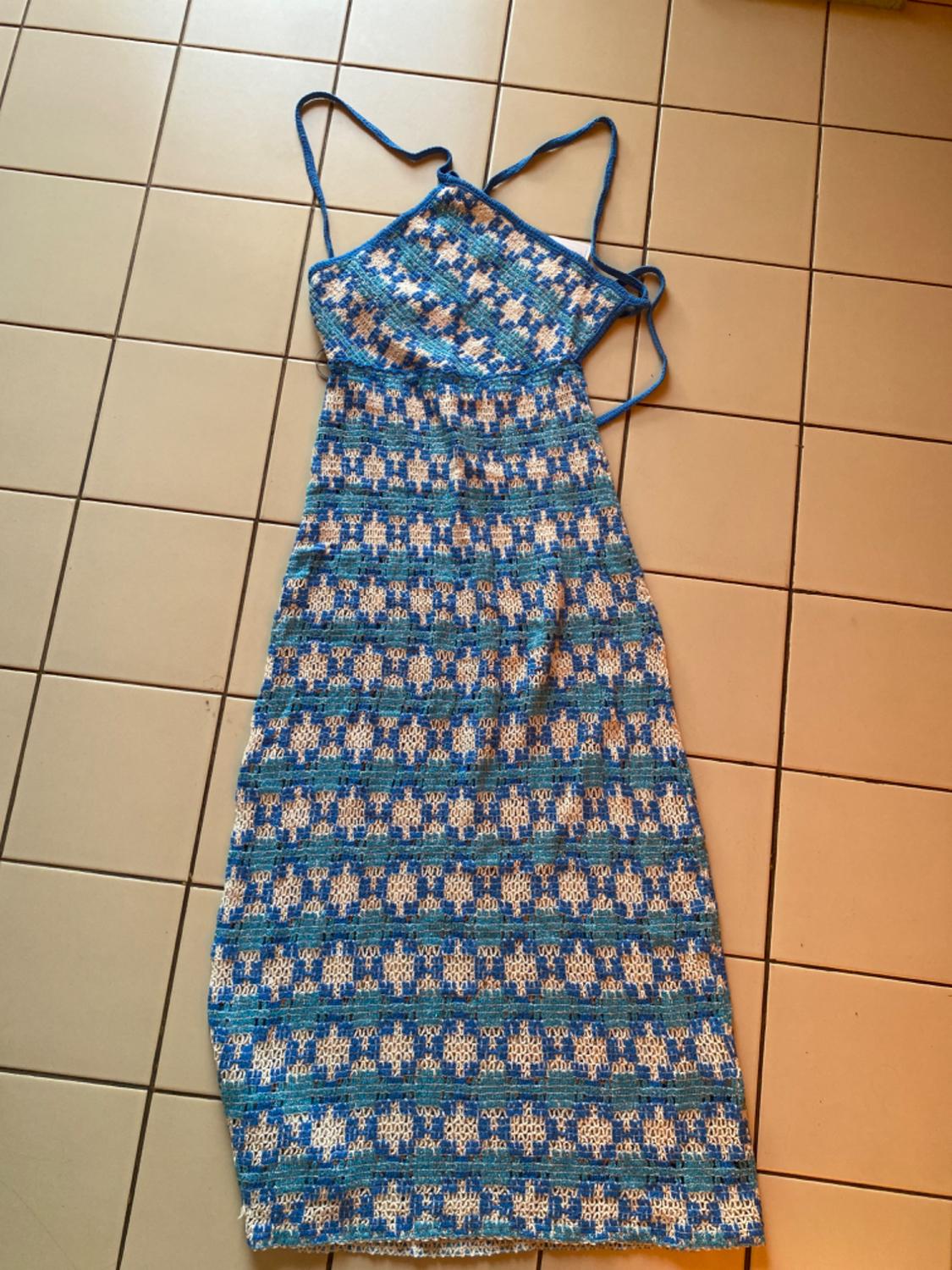 Blue and white knitted maxi dress with a geometric pattern, halter neck and thin straps, on a light tiled floor.