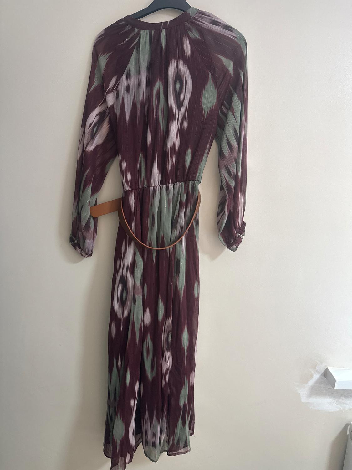 Long dress with an abstract print in burgundy and green tones, hanging on a black hanger against a white wall.