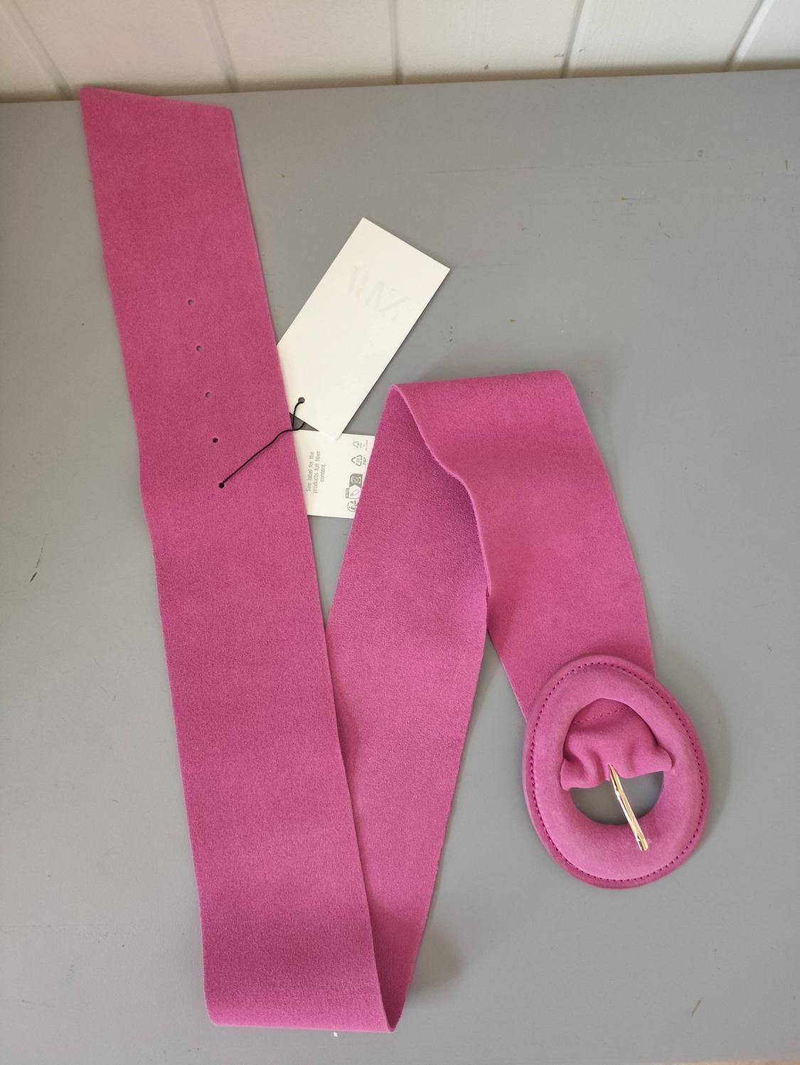 Wide pink belt with an oval buckle and a tag reading 'See label for the product's full fibre content', on a grey background.