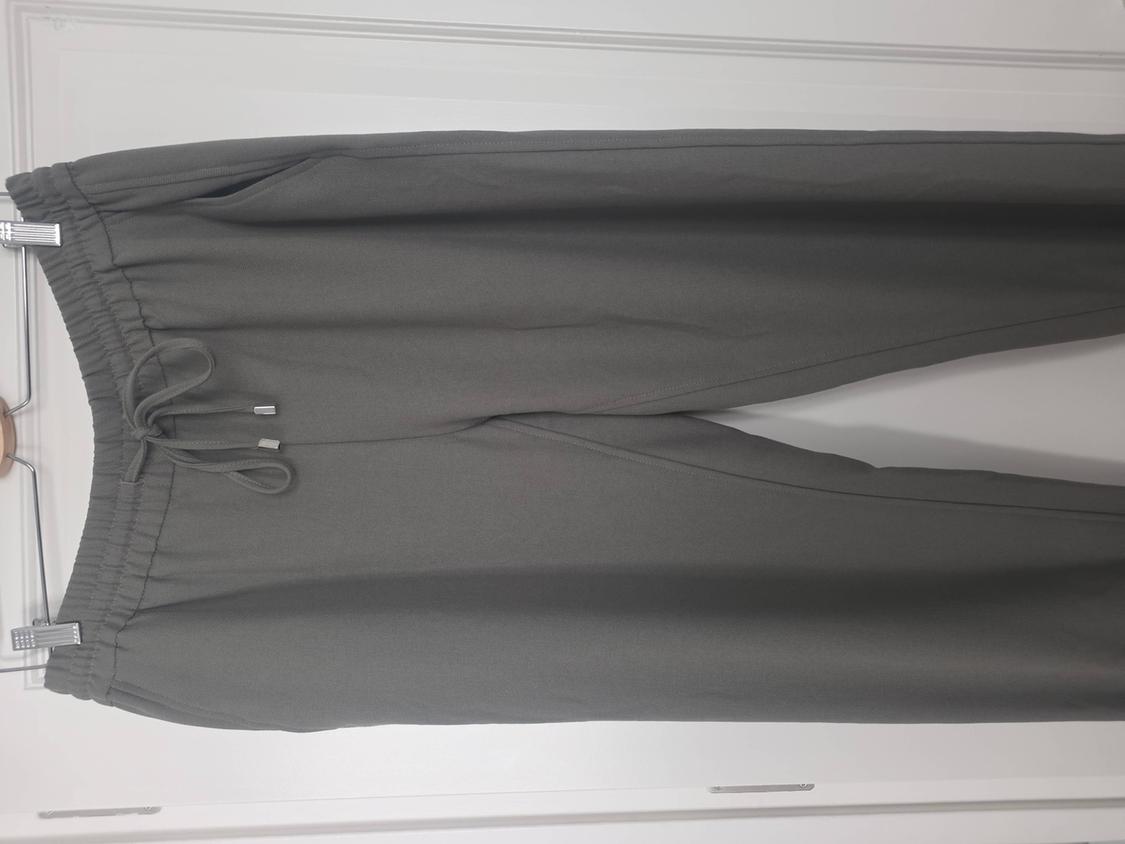 Grey trousers hanging on a hanger, with an elasticated waist and adjustable drawstring, against a white background.
