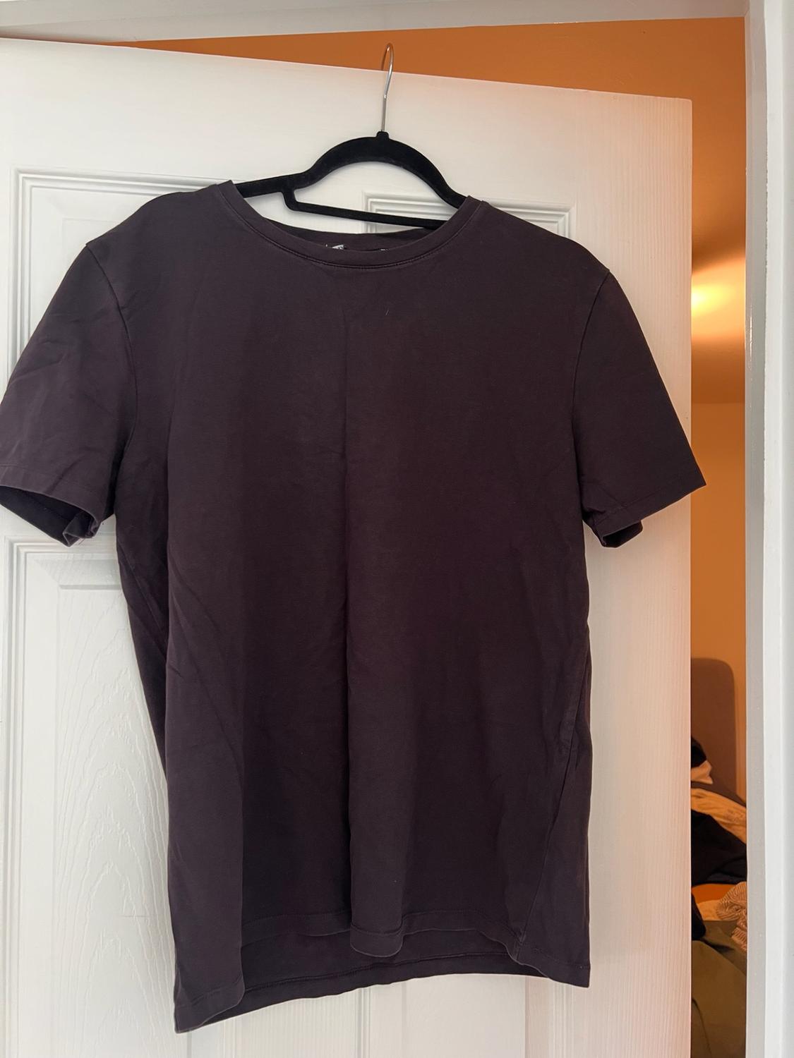Dark grey short-sleeved T-shirt on a black hanger hanging from a slightly open white door. Casual style in a relaxed setting.