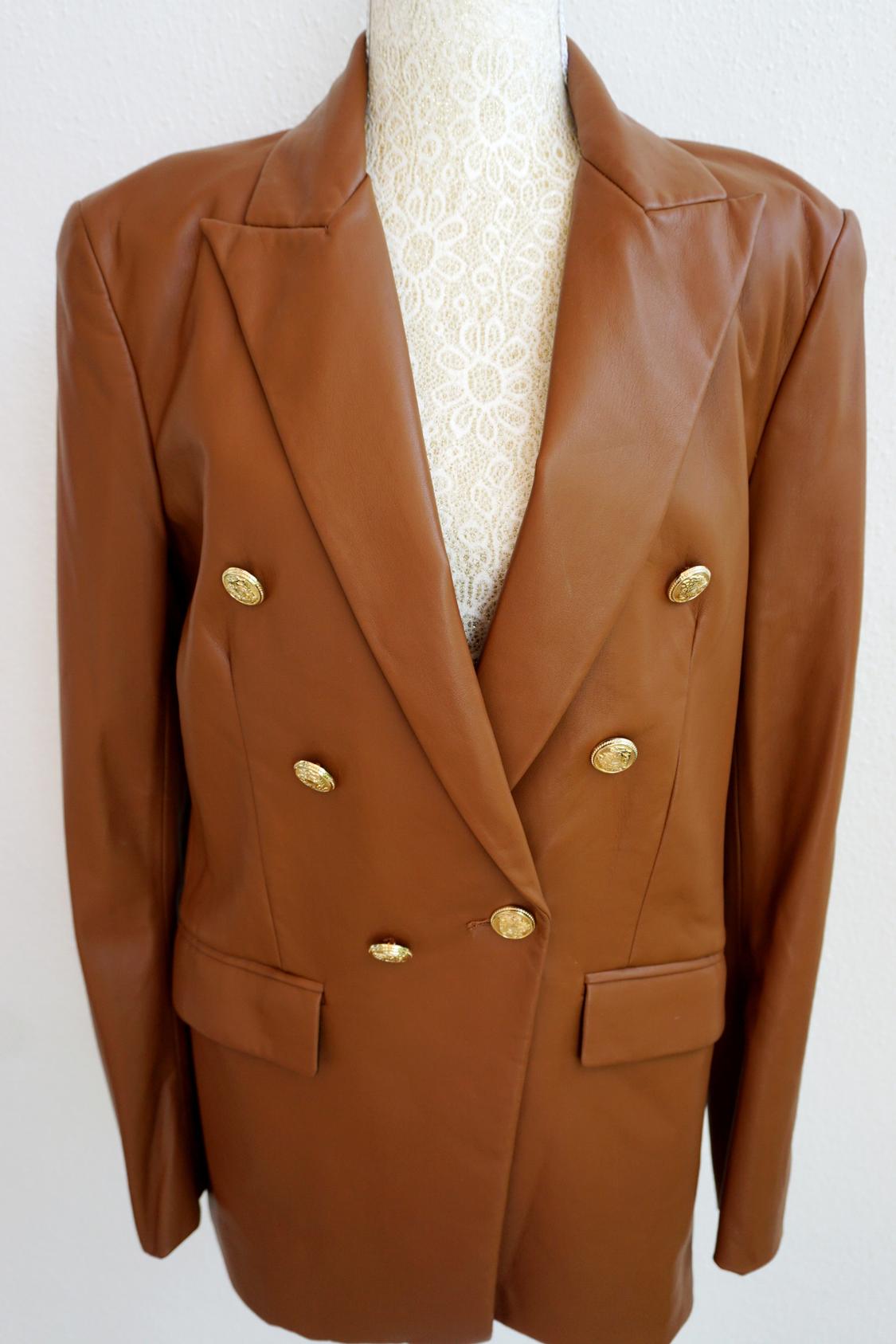 Brown double-breasted blazer with gold buttons on a mannequin with white lace in the background.