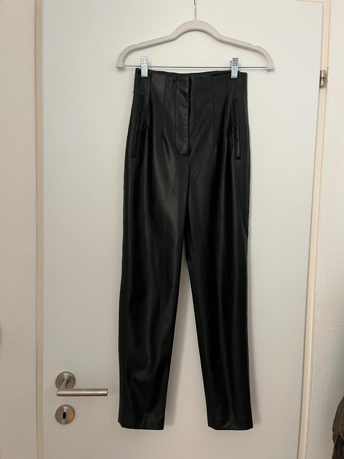 Black trousers hanging on a white hanger over a white door. Plain design with side pockets and a front fastening.
