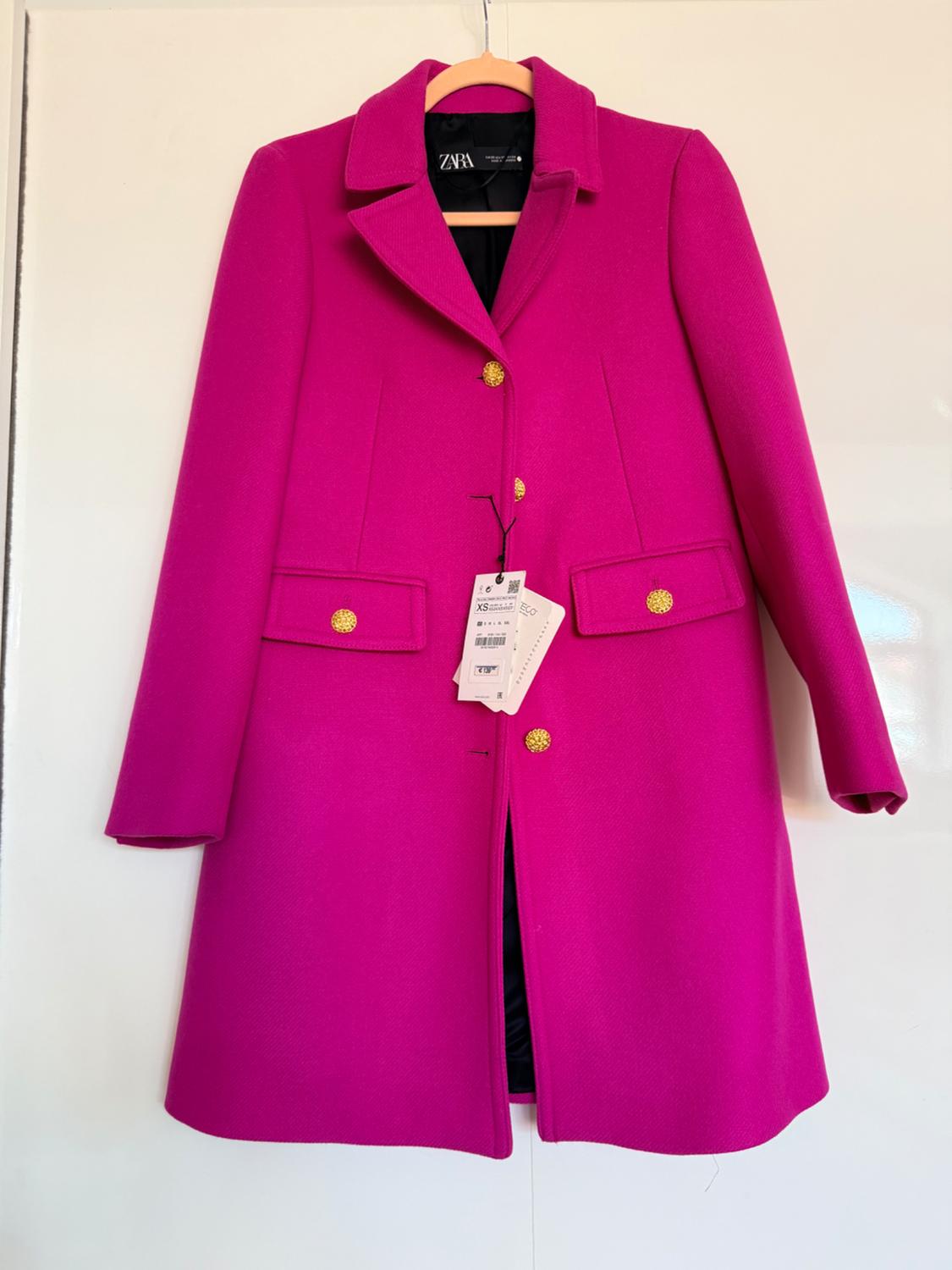 Fuchsia pink coat hanging on a wooden hanger. Notched lapel collar, gold buttons and pockets. Visible text: ZARA, XS.