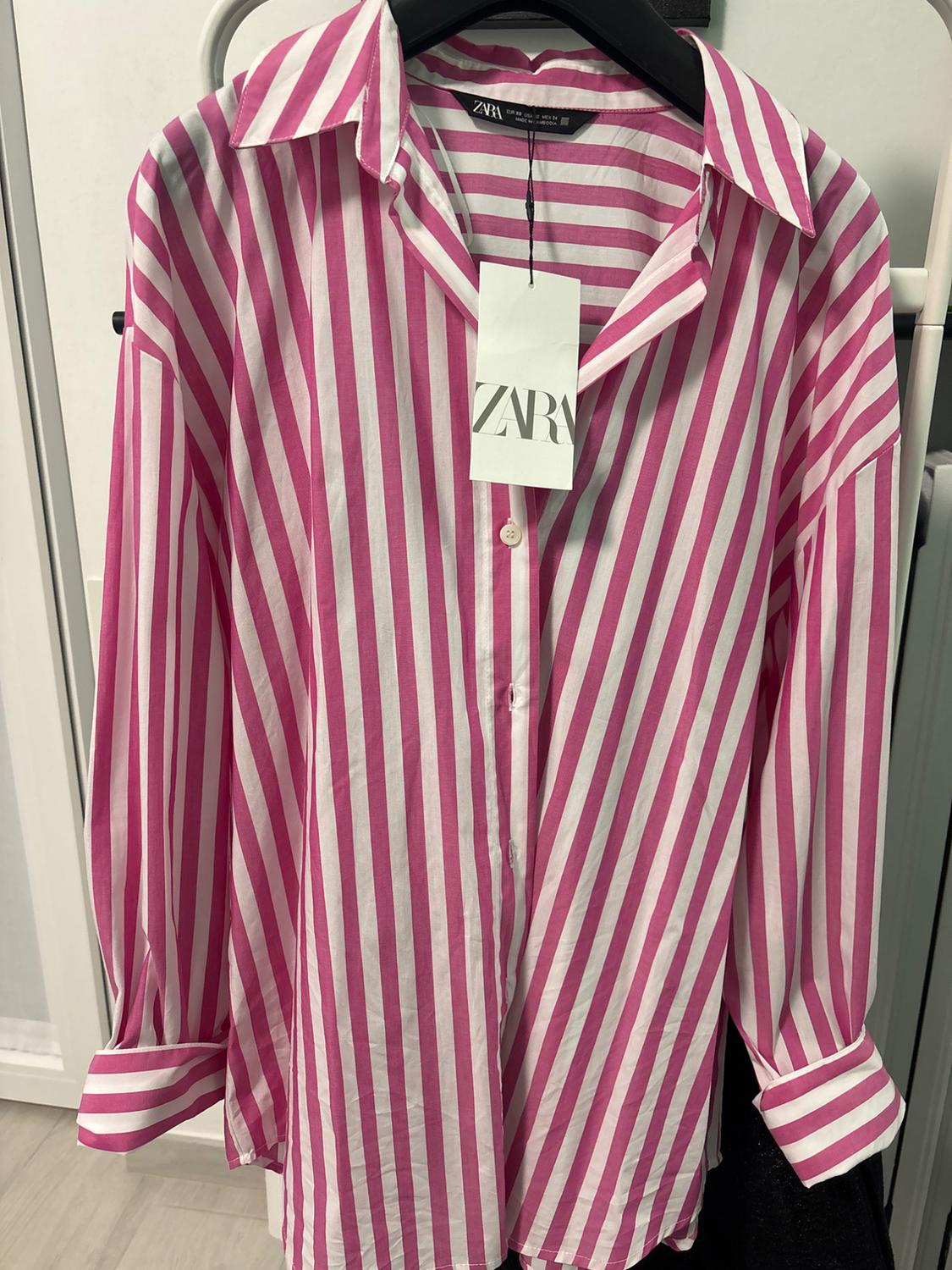 Shirt with vertical pink and white stripes hanging on a hanger with a Zara label visible on the collar.