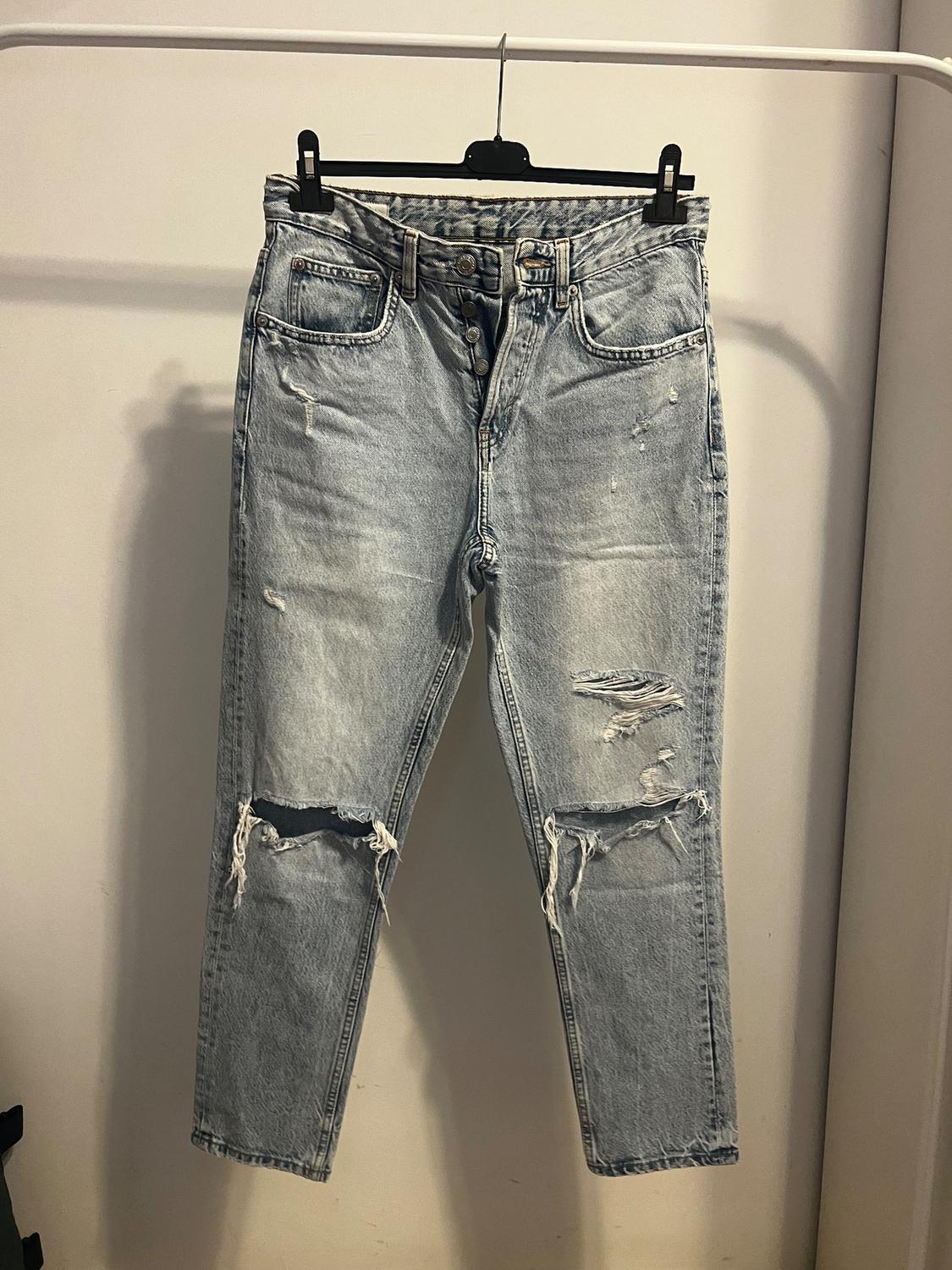 Light blue distressed denim jeans hanging on a hanger, with rips at the knees and frayed details.