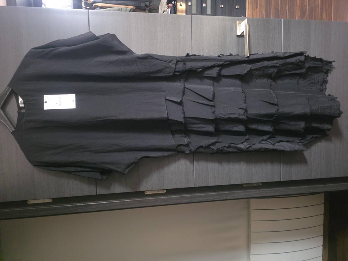 Black dress hanging in a grey wardrobe. Plain top and tiered skirt with frayed edges. White label visible.