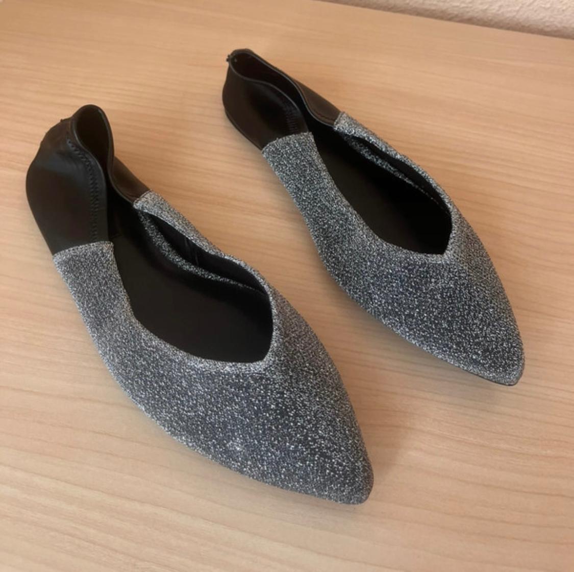 Black and shiny silver pointed flat shoes on a light wooden surface.