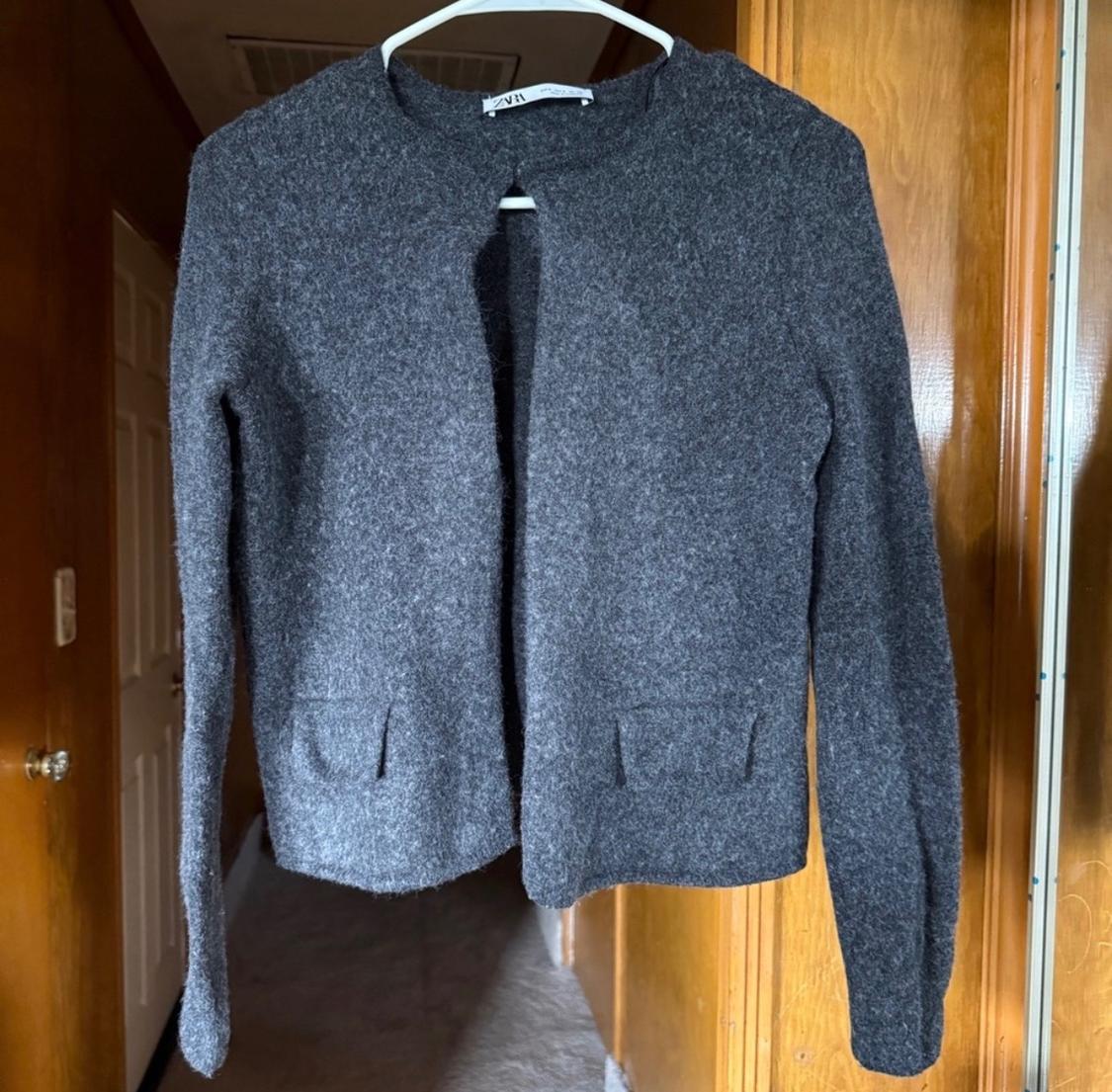 Gray wool jacket hanging on a white hanger, against a wooden background and white door. Visible label on the collar.