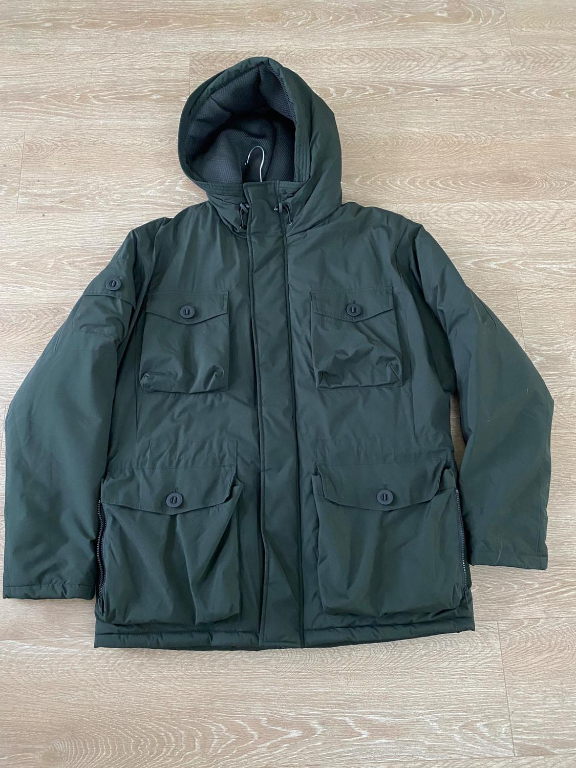 Dark green jacket with a hood and four button pockets, placed on a light wooden floor.