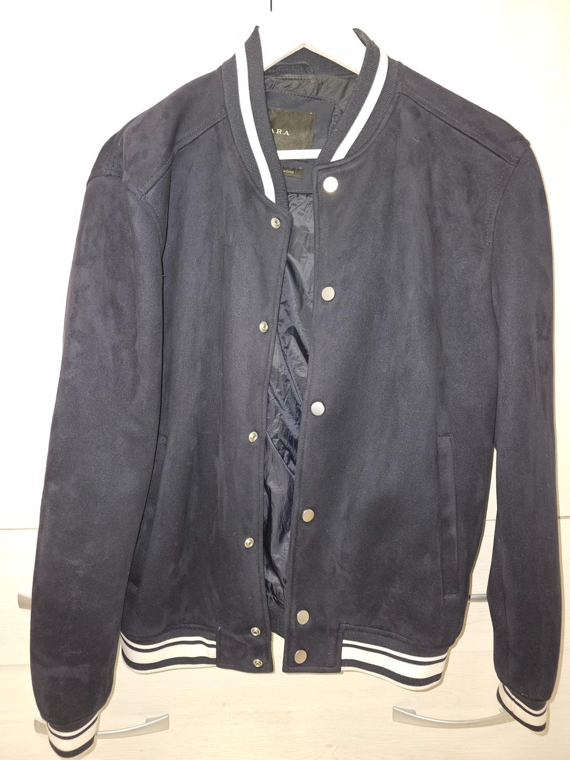 Dark blue varsity-style jacket with silver buttons and white trim on the collar, cuffs, and waist, hanging on a hanger.