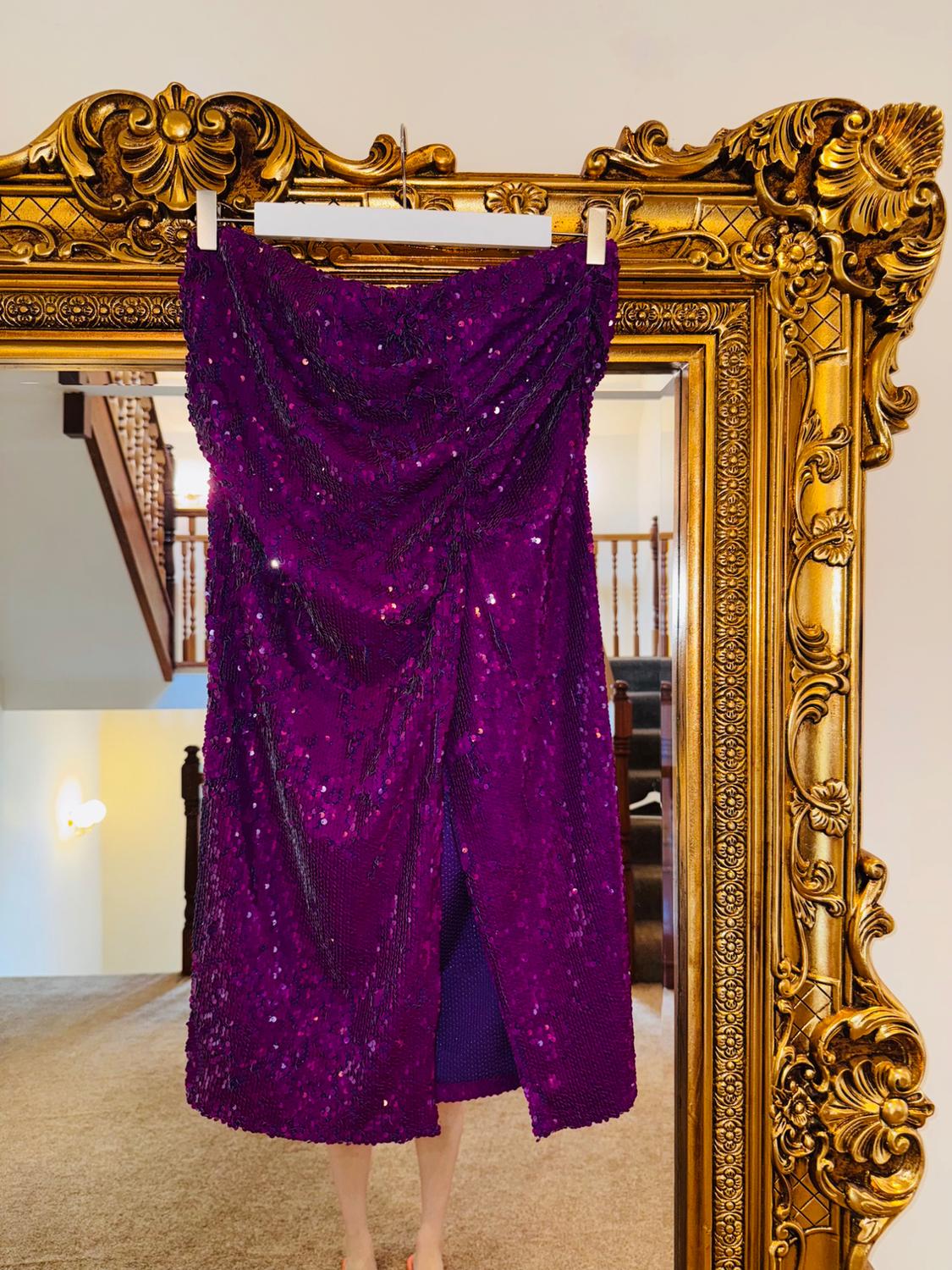 Purple dress with sequins hanging in an ornate gold frame. Reflection of stairs and beige carpet in the background.