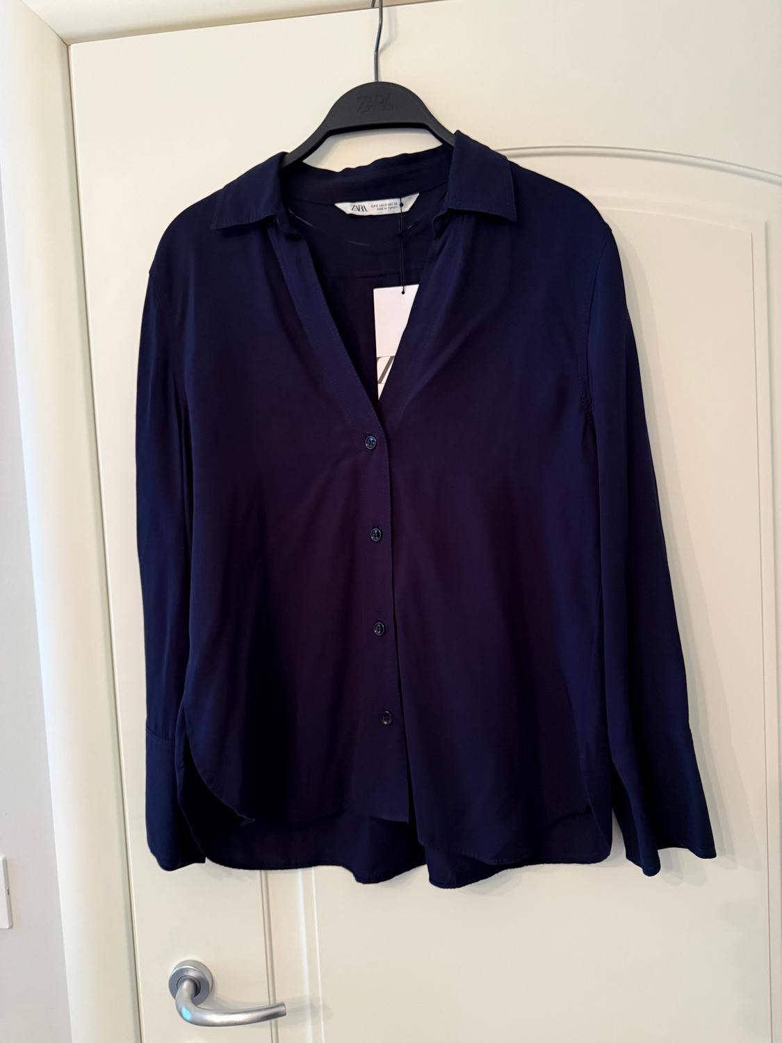 Navy blue long-sleeved shirt hanging on a black hanger over a white door. Label visible on the collar.