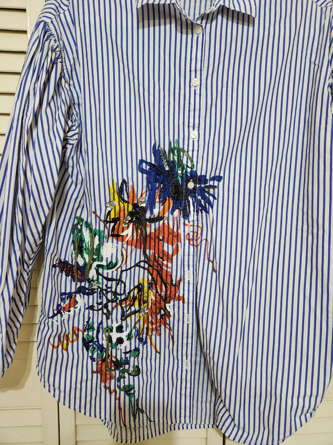 Front view of a blue striped shirt with a colorful graphic print on the chest.