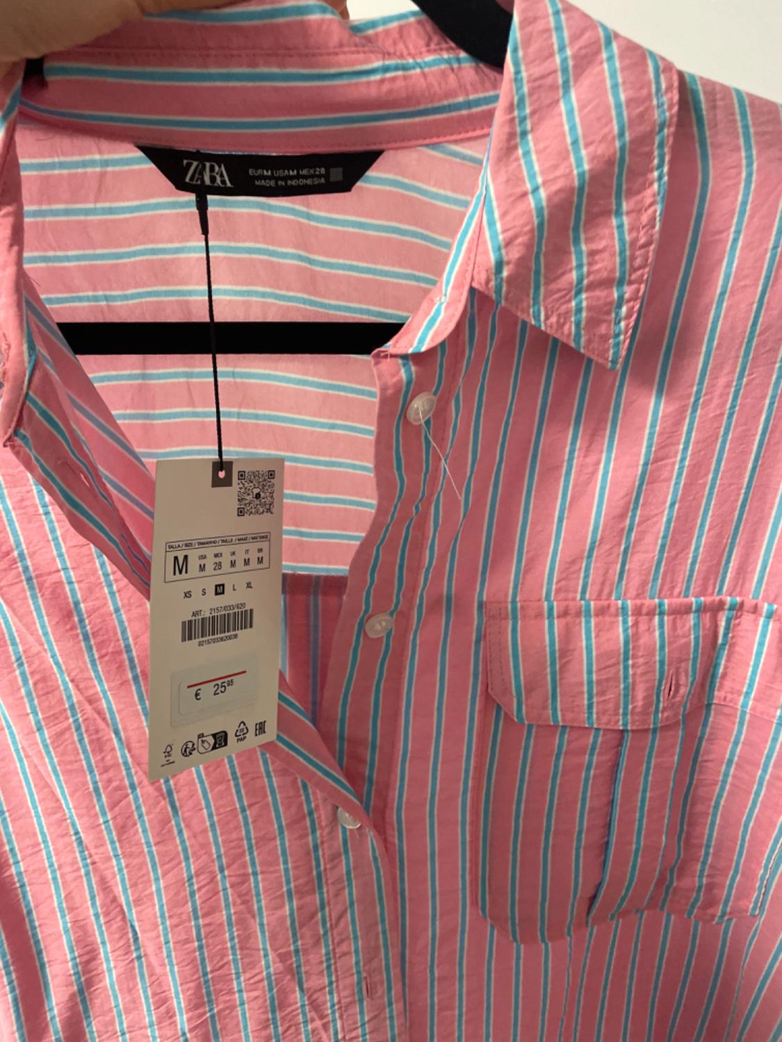 Pink and blue striped shirt hanging on a hanger, with a price tag of €25.95 and size M. ZARA brand, made in Indonesia.
