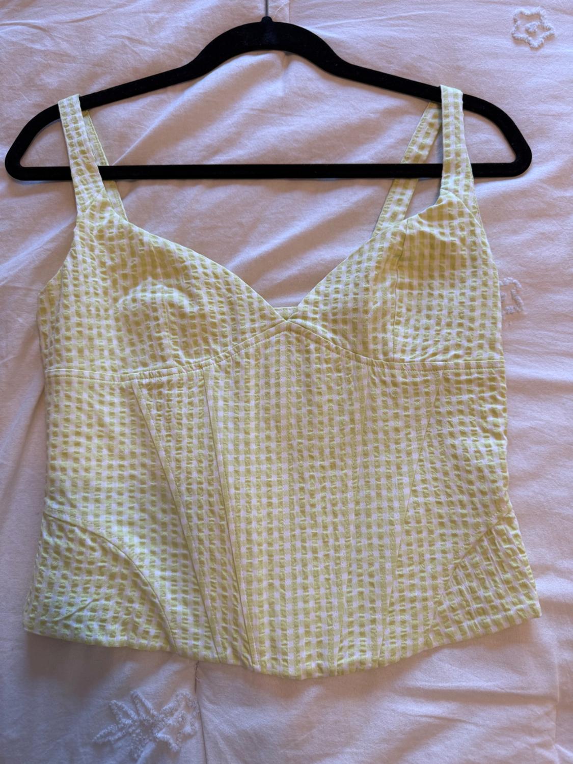 Green and white checked camisole top, hung on a black hanger over white embroidered fabric.