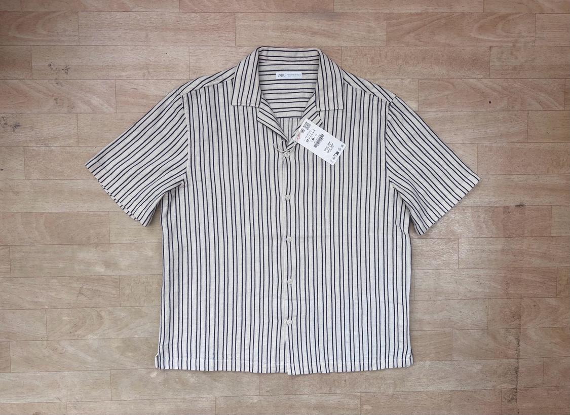 Short-sleeved shirt with vertical stripes and buttons, laid out on a wooden floor. Visible label with the text ZARA.