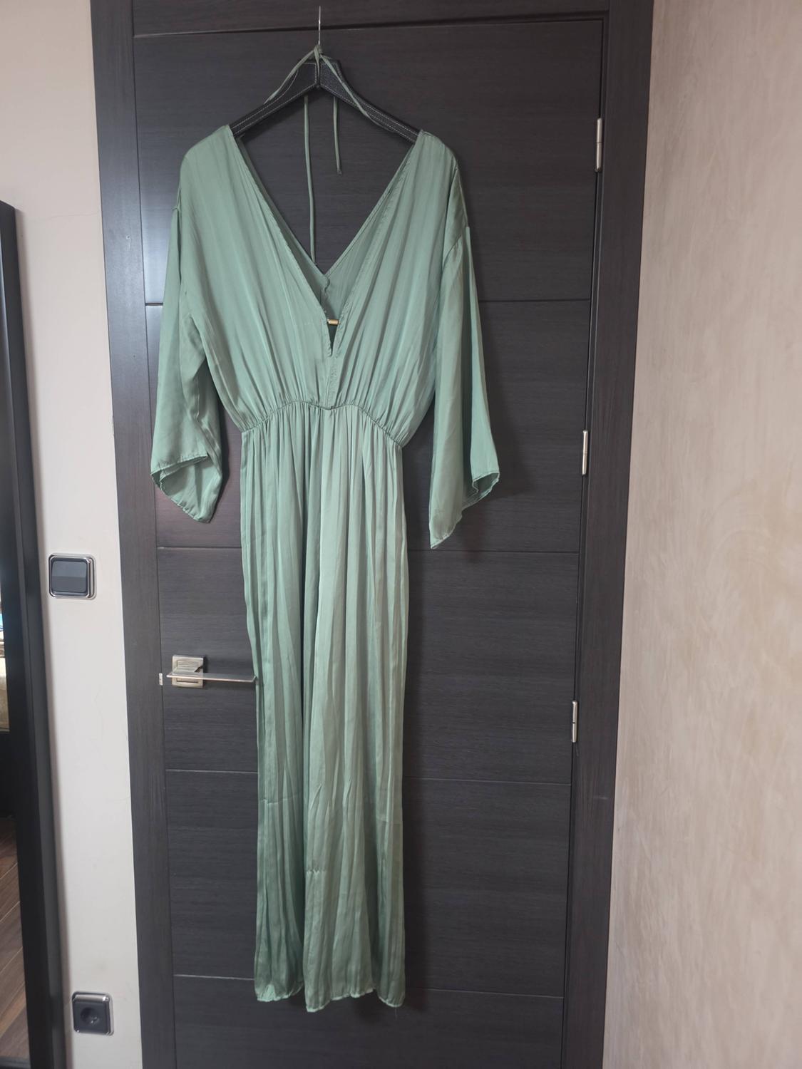 Light green maxi dress with a V-neck, fitted waist and wide sleeves, hanging on a dark door in a relaxed indoor setting.