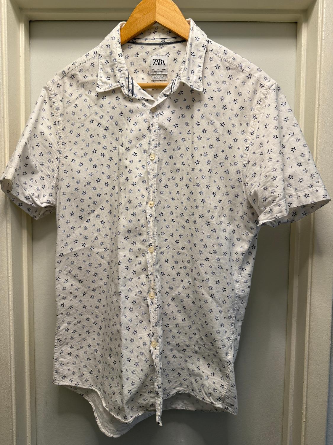White short-sleeved shirt with a small blue star print, hanging on a wooden hanger. Visible label: ZARA.