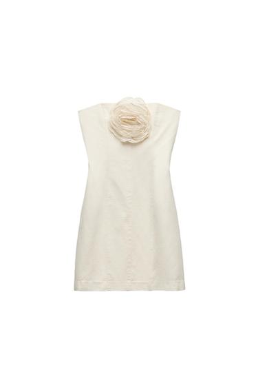 Ecru strapless short dress with a large fabric flower on the neckline against a white background.