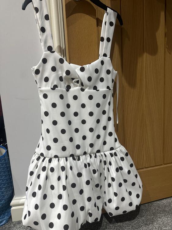 White dress with black polka dots hanging on a hanger. Wooden door and grey floor background.