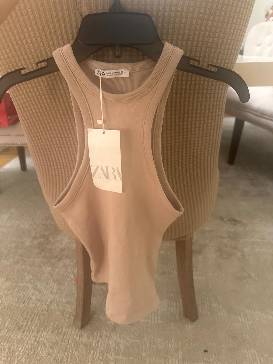Front view of a beige sleeveless t-shirt with a hanging tag.