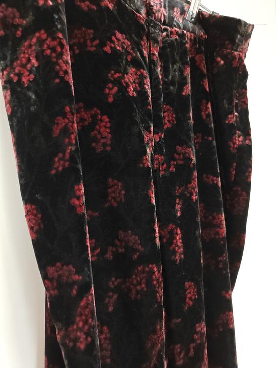 Black velvet trousers with a red floral print, hanging on a hanger against a white background.