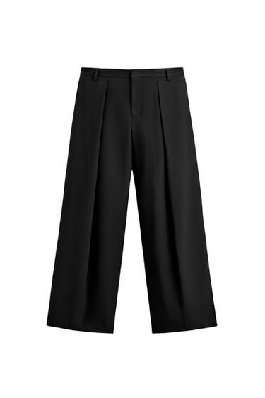 Front view of black wide-fit pants with front pleats, side and back welt pockets, zip and button fastening.