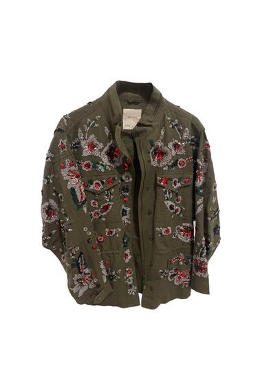 Olive green jacket with floral embroidery in red, white, and black. Visible label on the collar. White background.